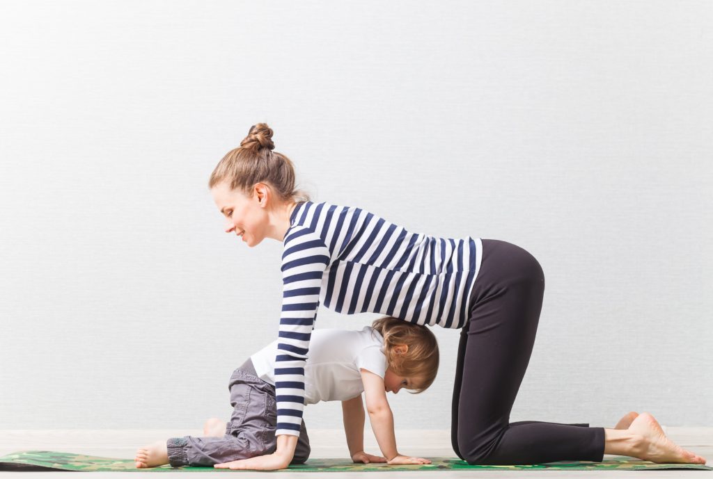 a mom and her child are on a yoga mat practicing tabletop pose on hands and knees