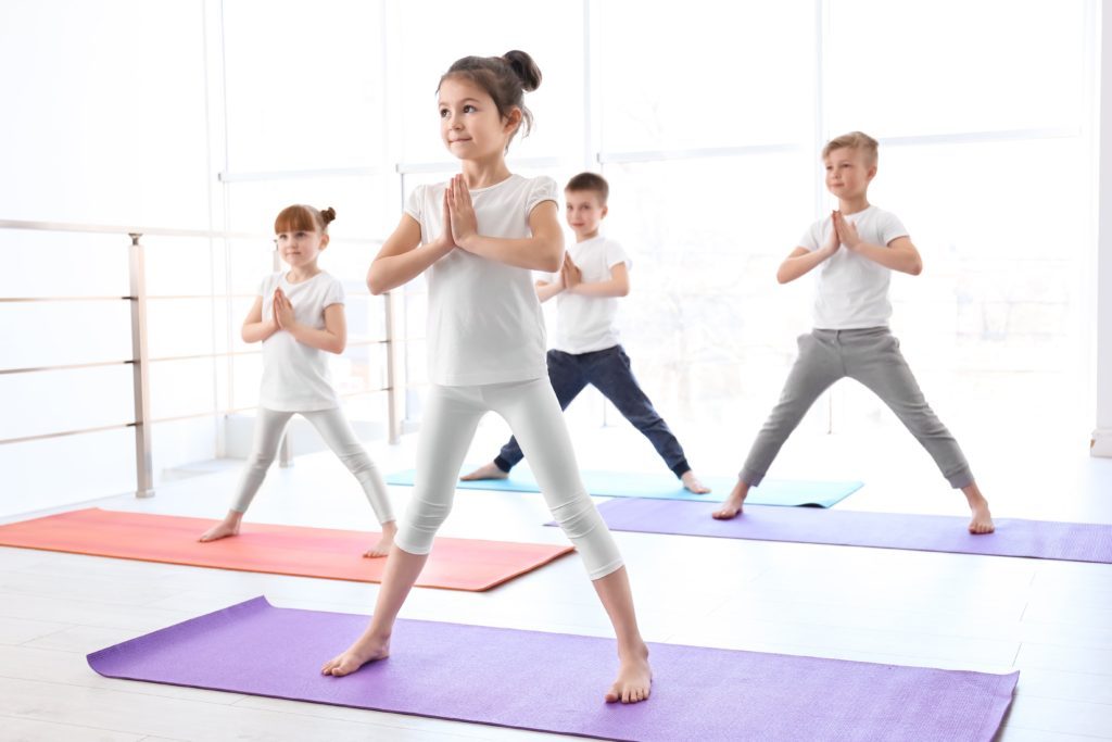 Four kids are practicing a wide legged yoga stance on yoga mats with hands at heart center