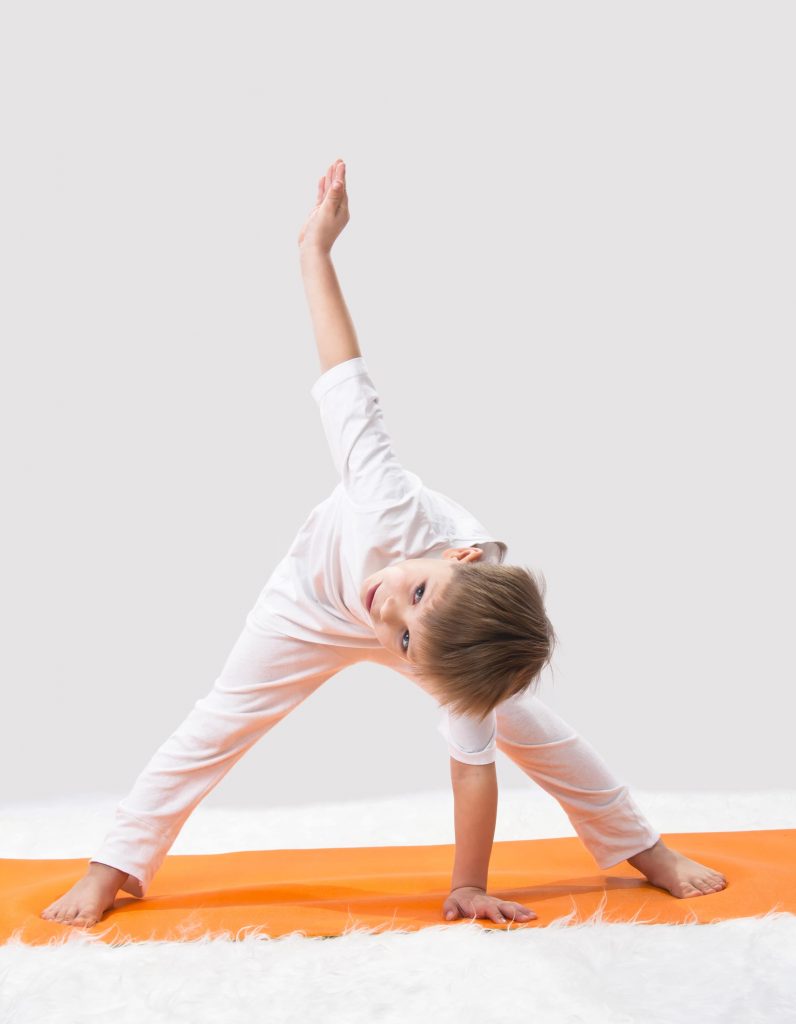 little boy doing wide legged forward fold twist yoga pose with one hand on an orange yoga mat and the other arm reaching up to the sky for movement-based brain breaks