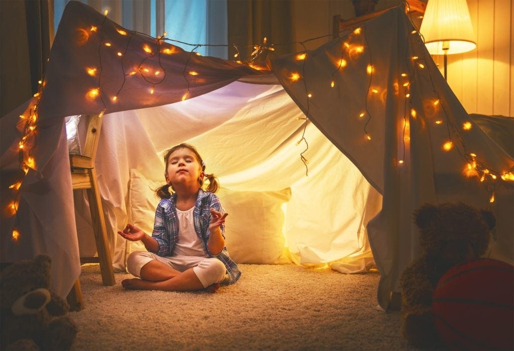 child girl playing meditates in yoga pose in tent at home before going to bed, mindfulness activities for kids, simple mindfulness activities