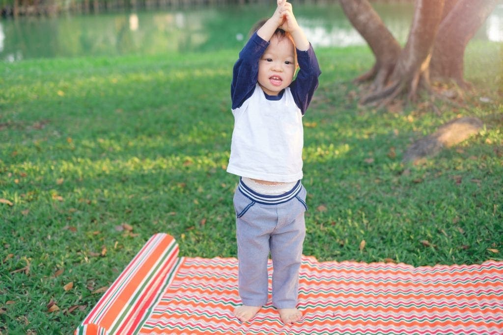 toddler mindfulness - mindful toddler lifting arms while outside practing a yoga mindfulness meditation game on a bright mat