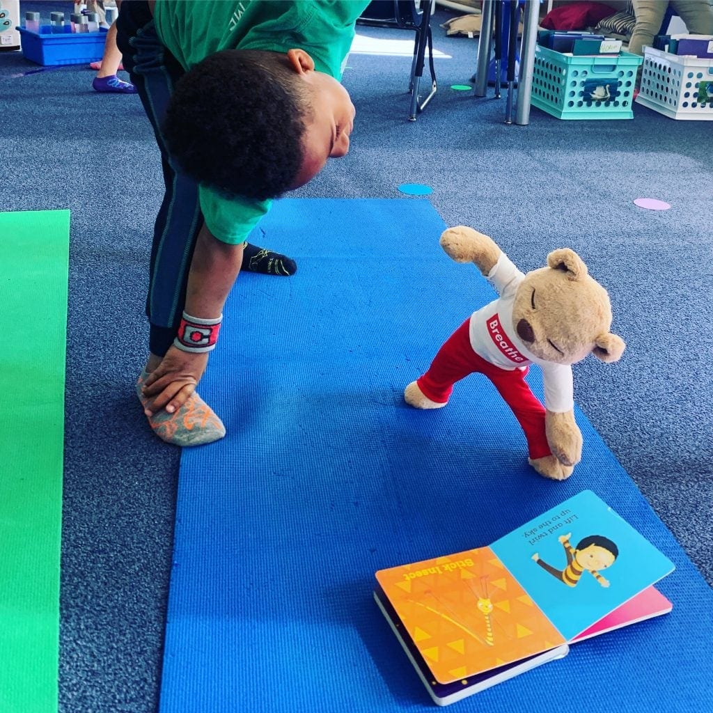 Meddy teddy is doing triangle yoga pose with a child on their yoga mat