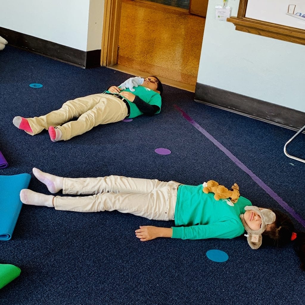 mindful students resting in a savasana pose and breating deeply with an animal on their tummy