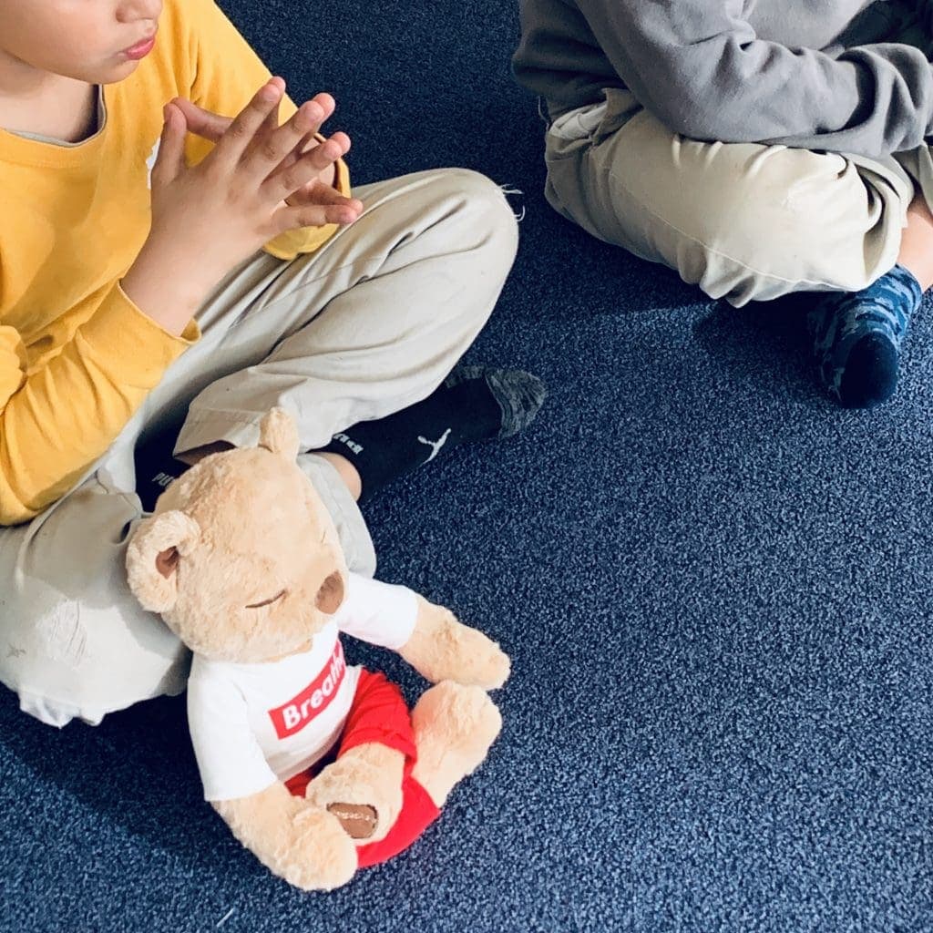 Meddy teddy is sitting next a student practicing mindful breathing and meditation