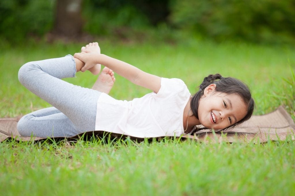 girl doing half bow pose on a yoga mat in a park, kids yoga classes