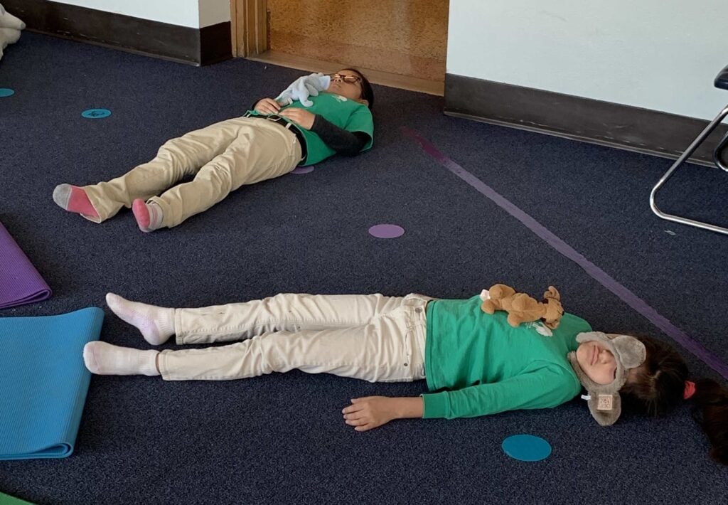two kids laying and resting in savasansa pose doing yoga in class