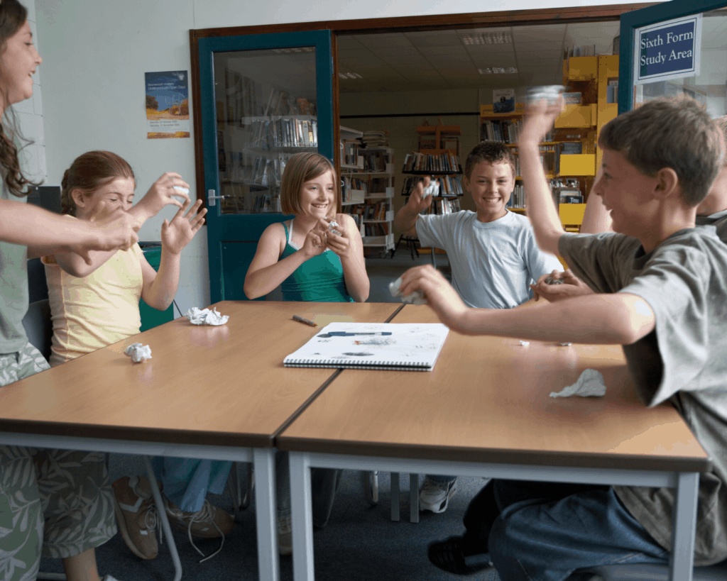 kids throwing crumpled papers across the room in a snowball fight - idea for winter-themed yoga game