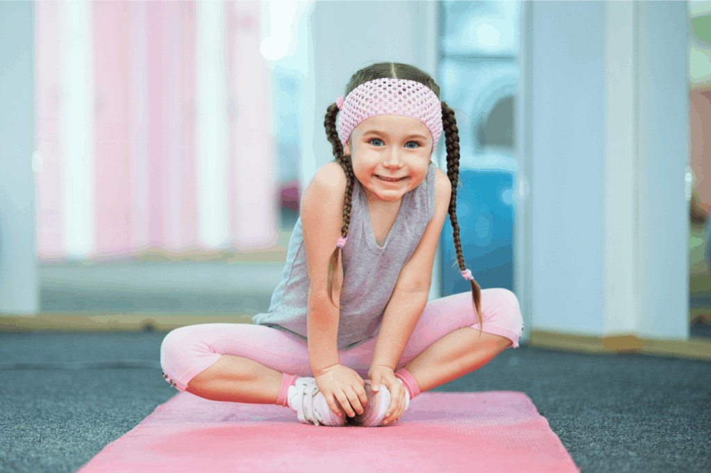 girl with braids and pink headband sitting in yoga pose on pink mat