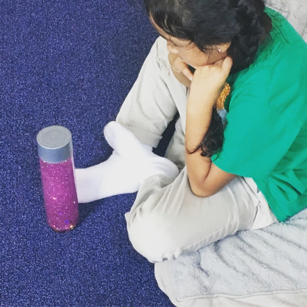 child sitting and looking at a mindfulness glitter calm down jar in school