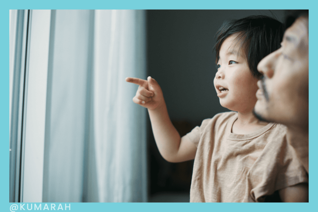 child looking at pointing at something with help of adult